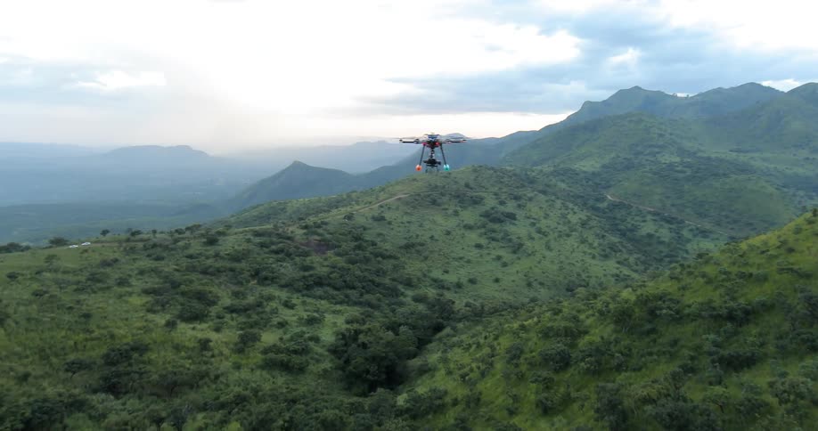 A drone is flying high in the air on a cloudy day