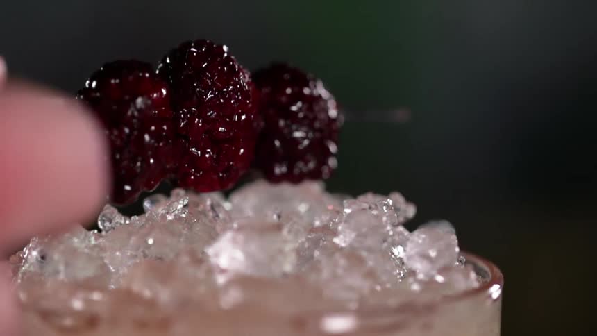 A cocktail filled with ice is garnished with a skewer of cherries