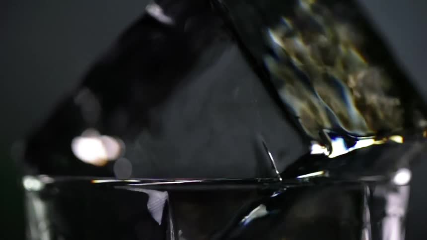 A sharp edged ice cube twirls around the rim of a shot glass