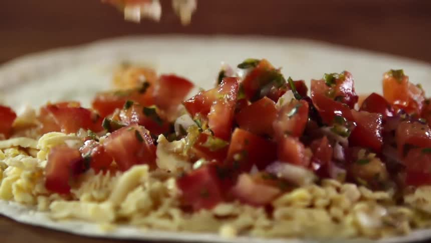 Diced tomato with green herbs are dropped onto a plate