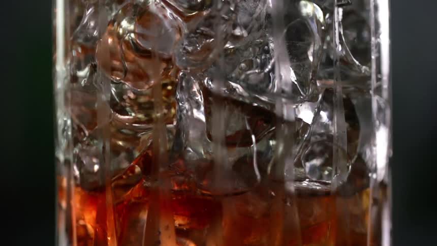 A glass is packed with ice and a dark alcoholic beverage is slowly poured over the ice