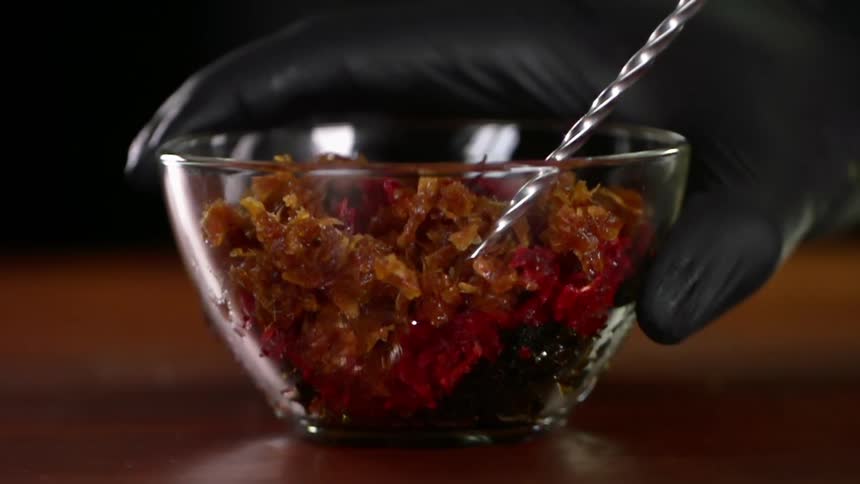A person stirs a bowl of hookah tobacco with different flavours
