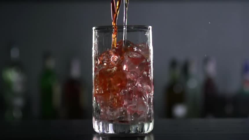 Red and white alcohol is being poured into a glass with ice cubes in a bar