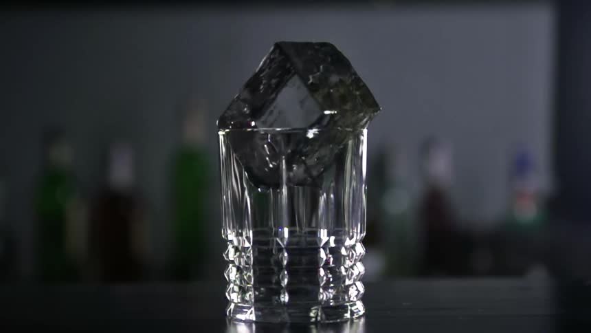 Large ice cube spinning on a shot glass with bottles in the background