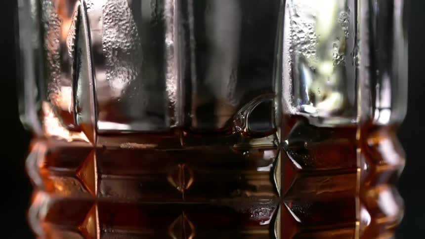 Amber liquor is being poured into a glass on dark background