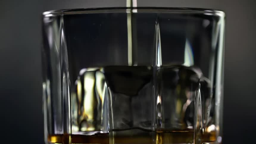 Yellow alcoholic beverage pouring over ice inside a glass against a dark background