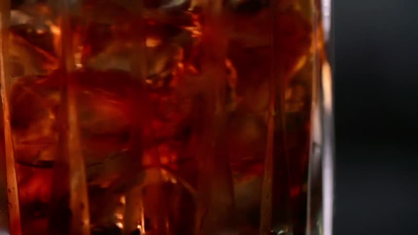 An amber alcoholic beverage with ice cubes stirred in a glass