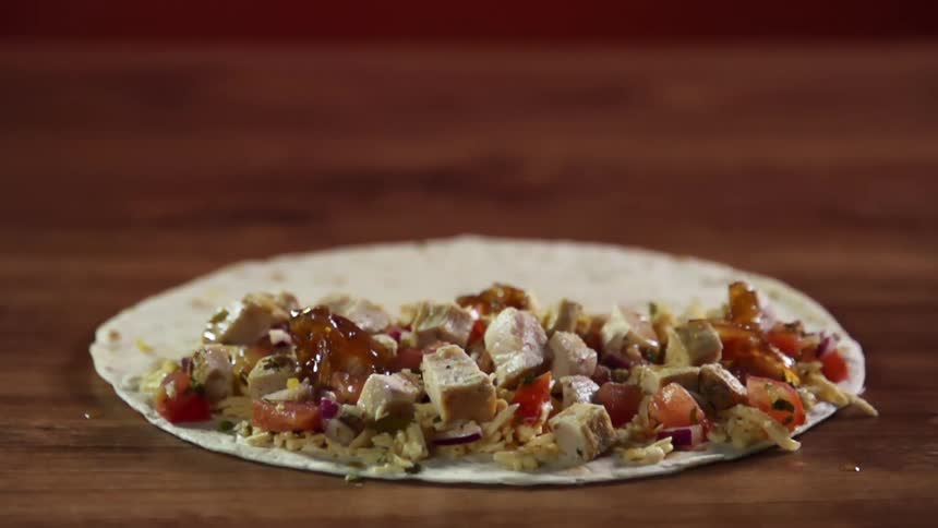 Pouring jam over the filling of a flour tortilla on the surface of a wooden table