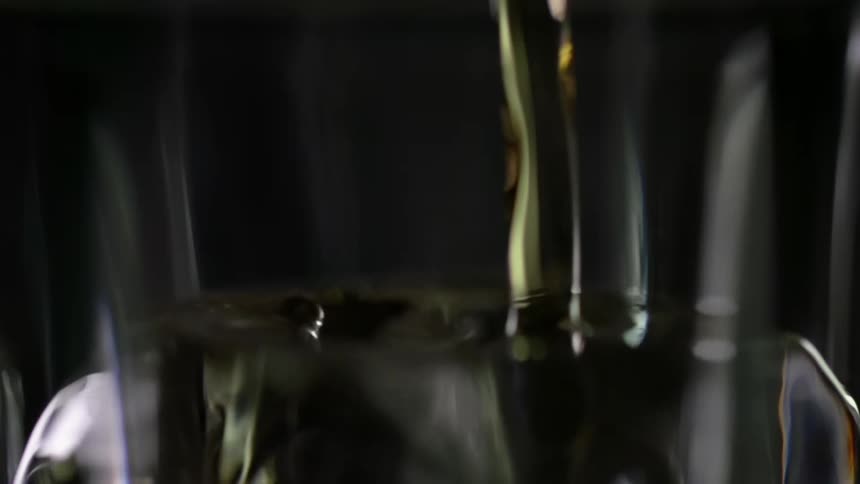 Yellow alcoholic beverage pouring over ice inside a glass against a black background