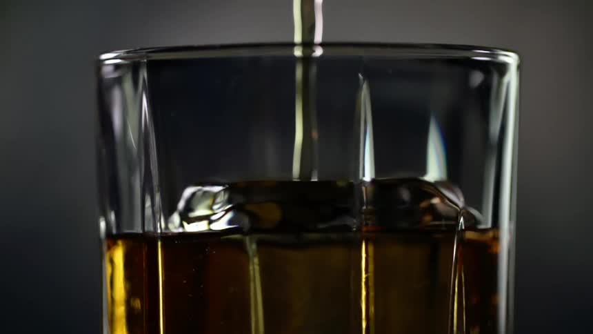 An alcoholic beverage is poured into a glass of ice