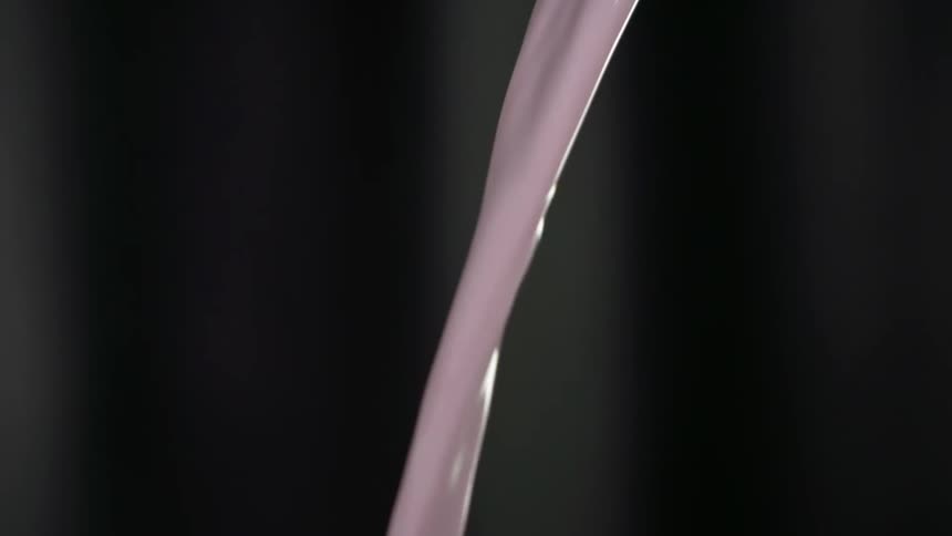 Purple cocktail being poured into a glass with a dark background