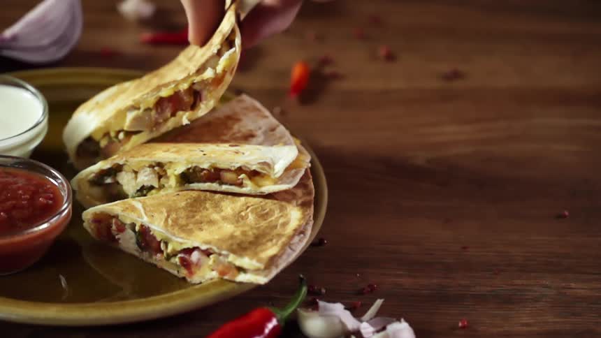 A person lifts a slice of a quesadilla from a plate with two fingers