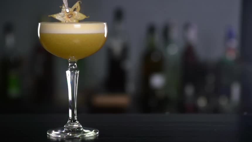 A piece of star fruit being placed on a cocktail on a bar top
