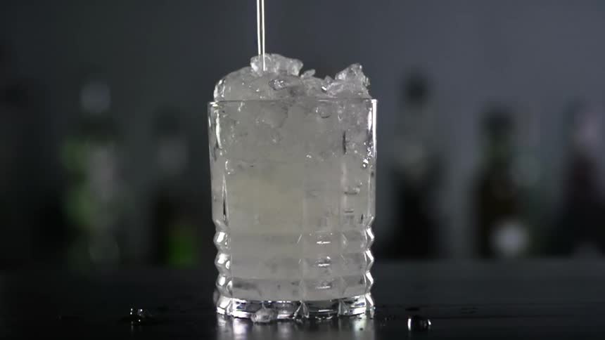 Cocktail is poured onto ice in a glass tumbler in a bar