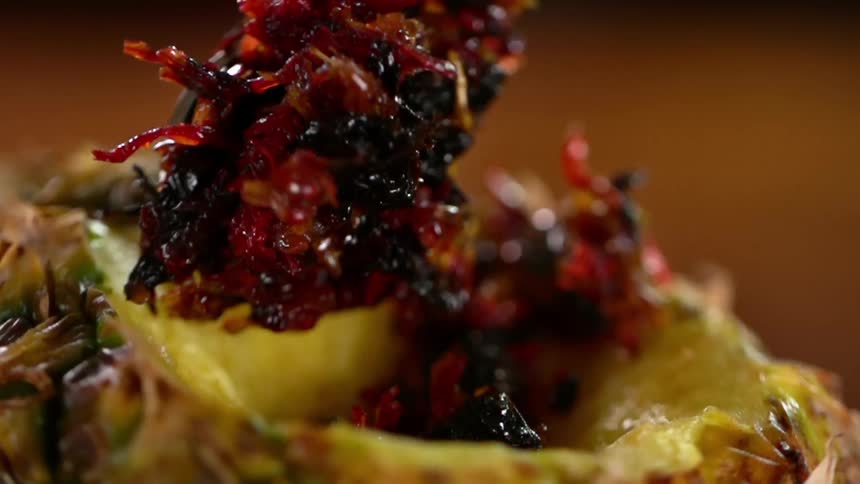 Tobacco falls from a spoon into a pineapple used as a bowl