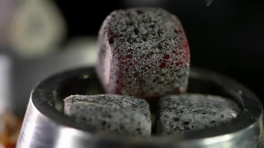 A small cube of charcoal is placed atop a metal ring with two other cubes of charcoal