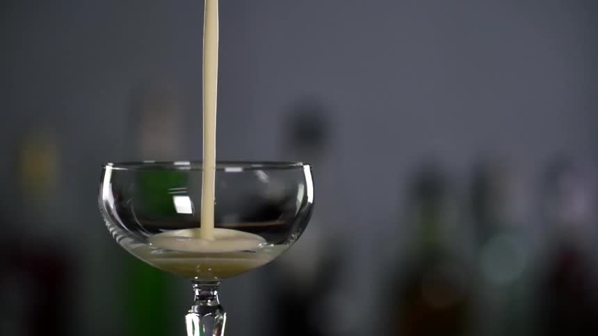 A thick yellowish white liquid is being poured into a glass in front of bottles