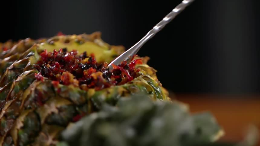 A stainless stirrer is used to stir tobacco that fill the side of a pineapple bowl