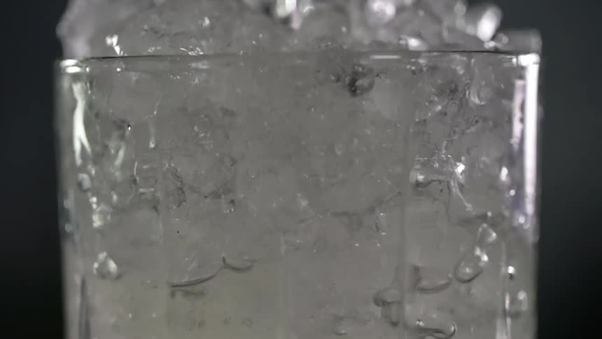 Close up of a liquid being poured into a glass with ice cubes in studio