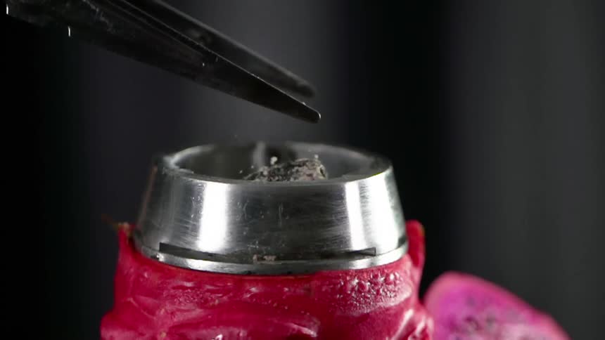 A tweezer putting a piece of charcoal in a metal ring