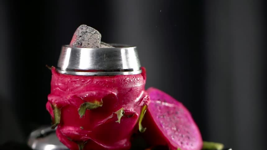 A dragonfruit is used to cover a metal cup containing heated charcoal