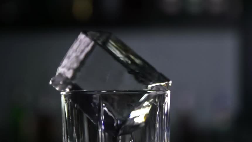 Large ice cube reflects light while spinning in the rim of a glass