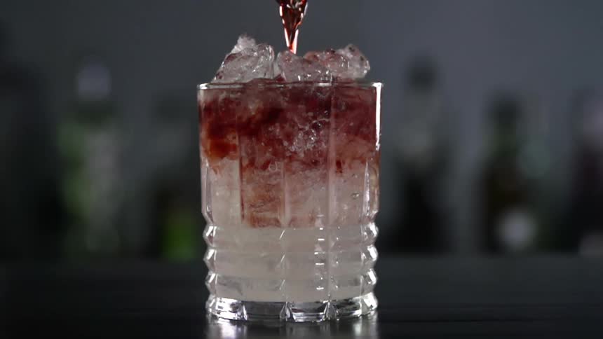 Red alcoholic beverage is being poured into a glass with ice cubes