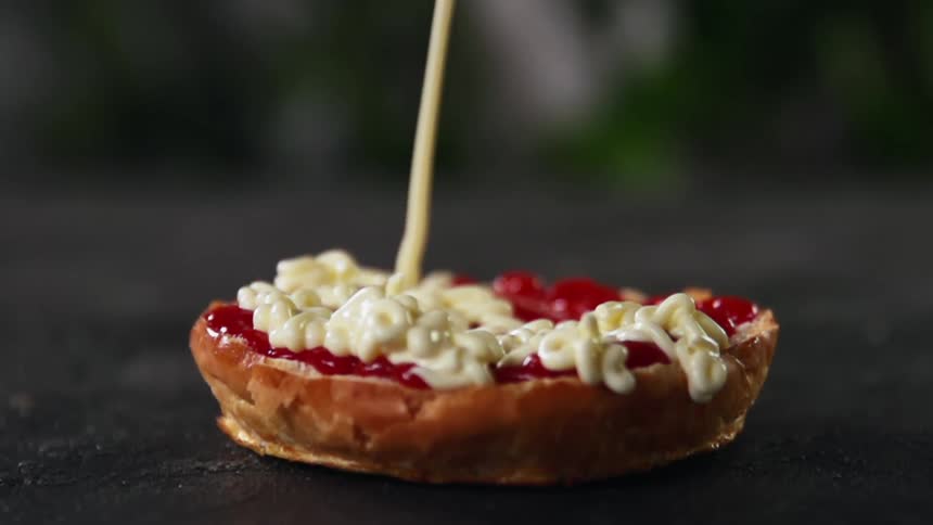 Mayonnaise is slowly drizzled atop a sliced bun that is already coated with ketchup