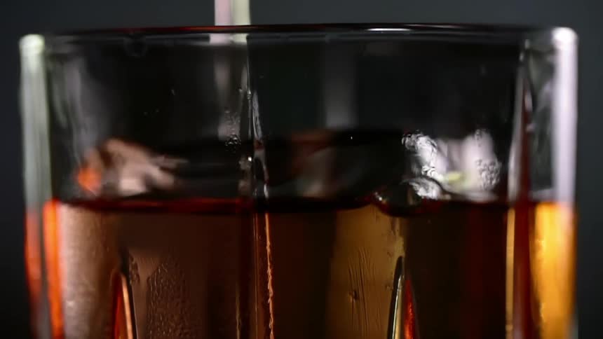 Cocktail is being poured into a glass with an ice cube