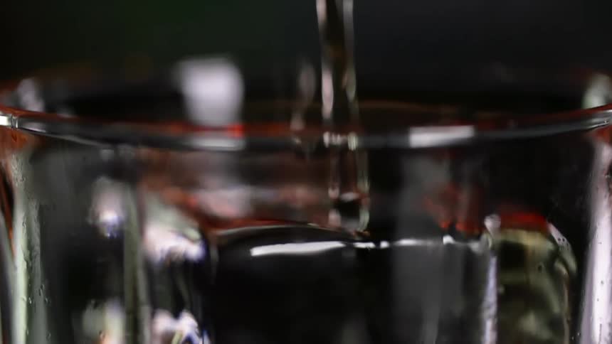 Cocktail being poured over a large ice cube in a drinking glass