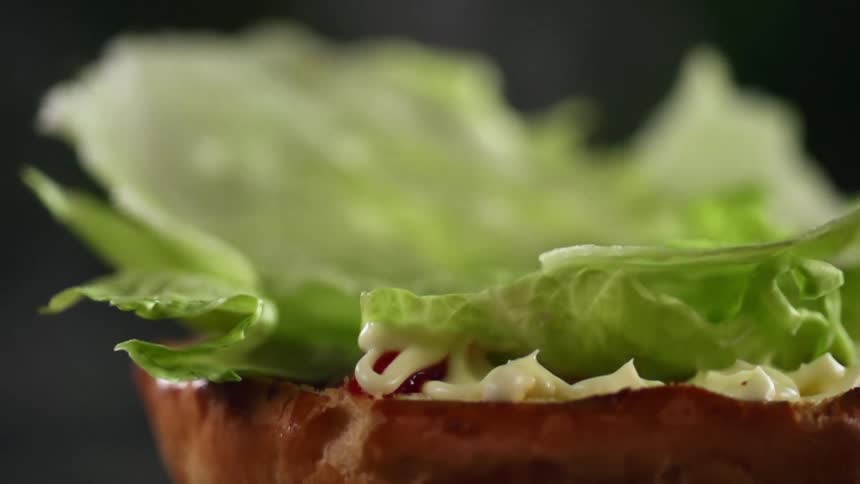 Lettuce falling onto a bun with spread over it