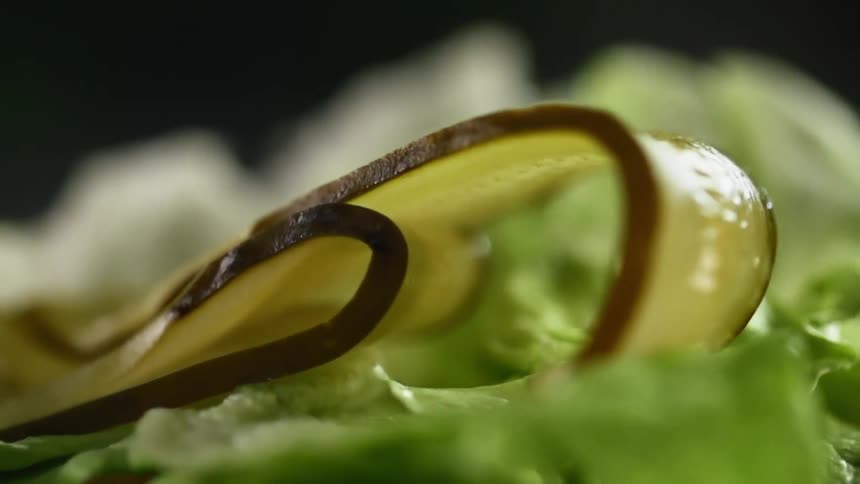 Two thinly cut slices of pickle are dropped onto the top of a pile of lettuce