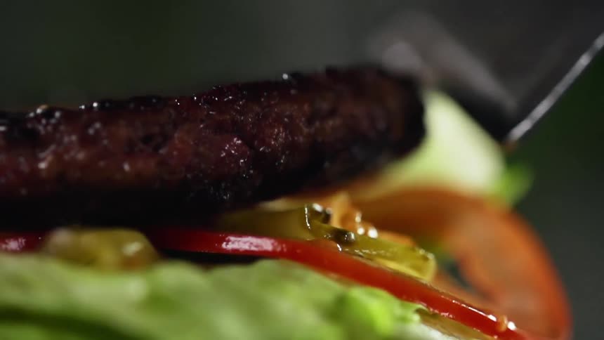 A burger patty  is placed onto the lettuce and tomato slices