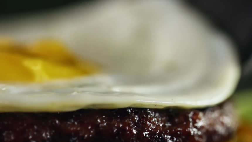 A fried egg being placed atop a burger patty