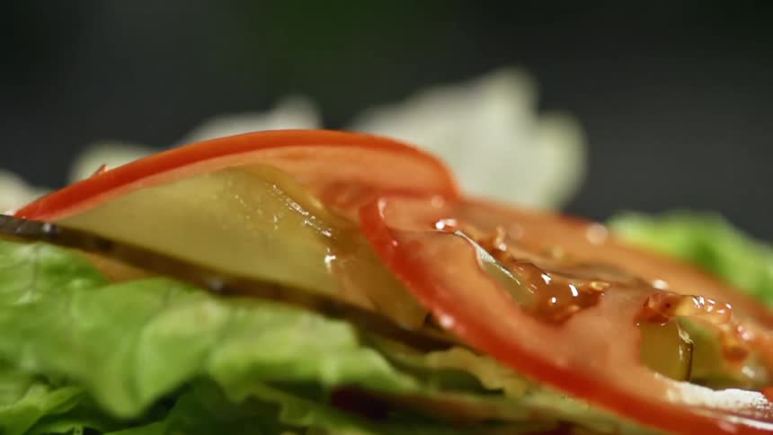 Tomatoes falling onto lettuce and pickles