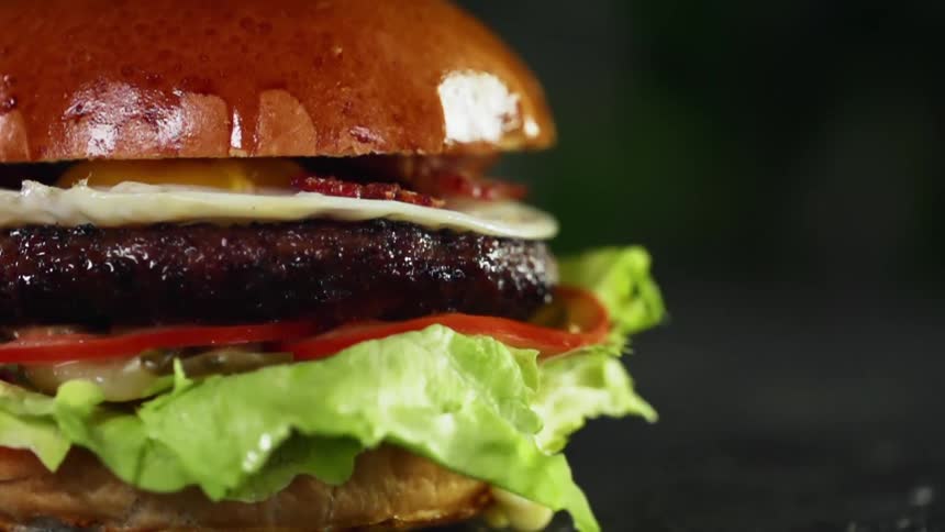 The top of a brioche bun falling onto a burger