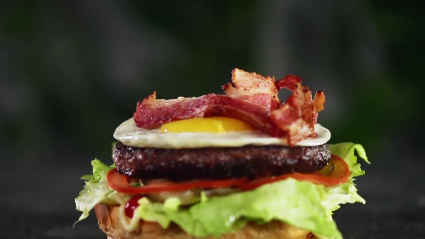 Bacon slices are dropped onto a burger with fried egg