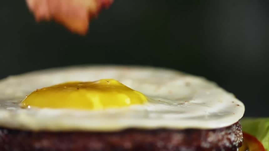 Pieces of bacon added to the top of a fried egg that is sitting on a hamburger patty