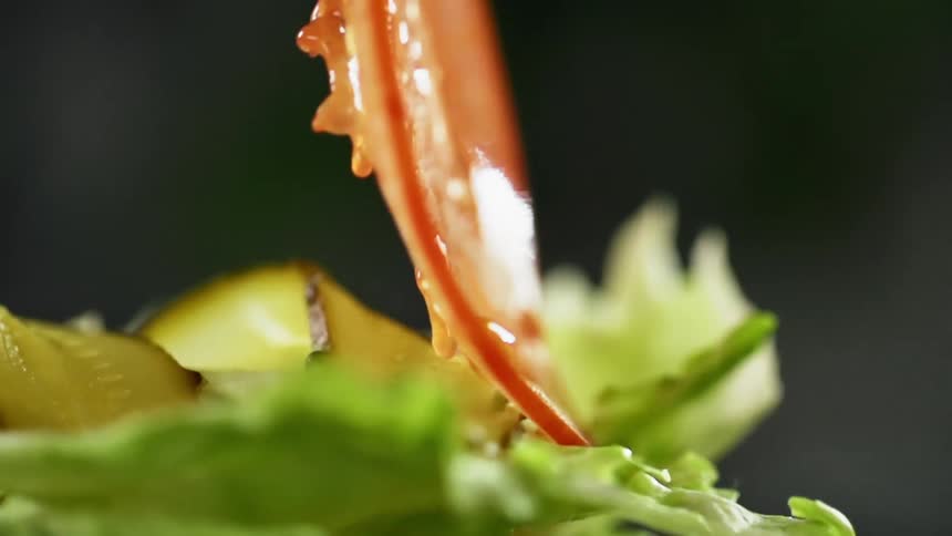 A tomato being placed on lettuce and pickles during a photo shoot