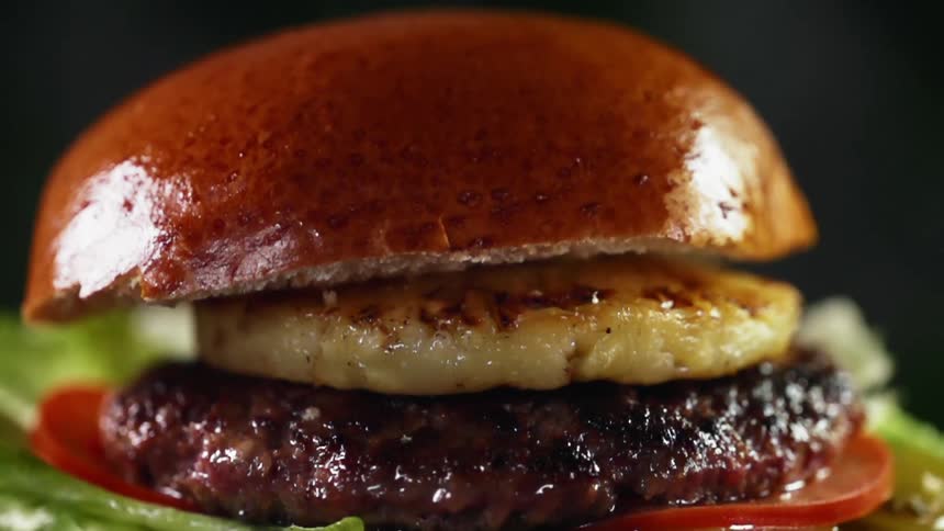 Close up of top bun being dropped on a juicy hamburger with a slice of grilled pineapple