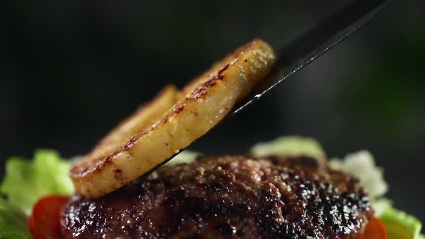 A slice of cooked pineapple laid on top of a hamburger patty