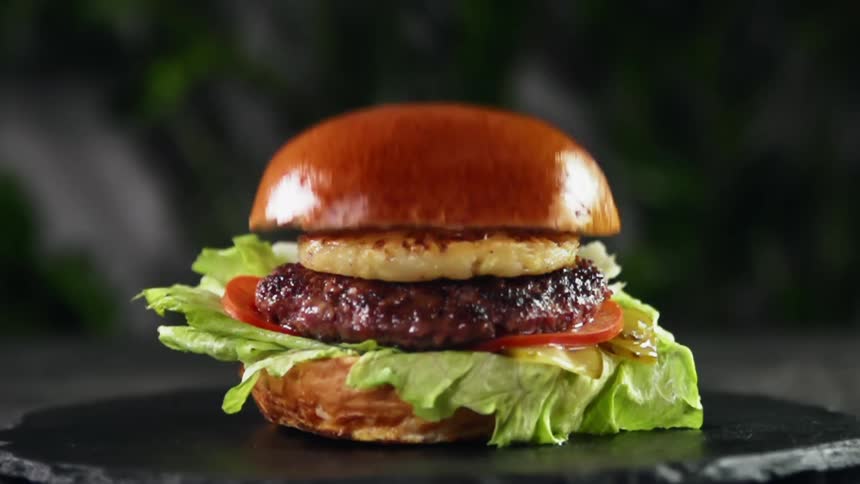 Juicy burger with tomato slice pineapple slice and lettuce between two halves of a bread roll is ready to serve