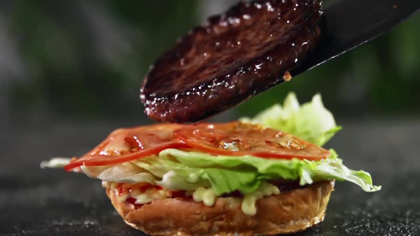 A juicy burger patty is being put on tomato slices and lettuce to make a hamburger