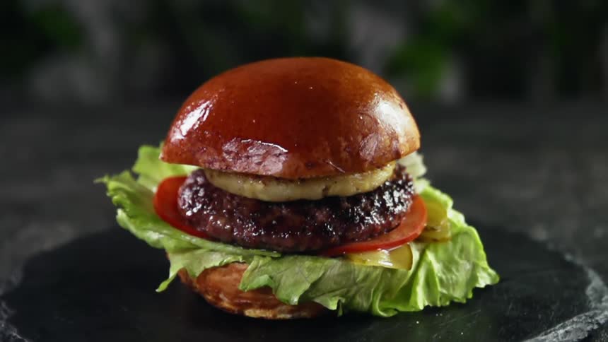 The top of a bun drops on to a hamburger set up for a photo shoot