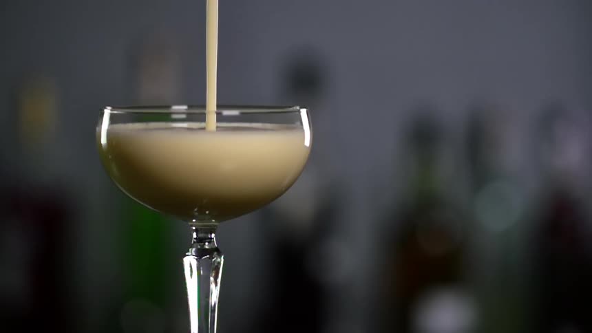 Cocktail is being poured into a glass in front of bottles