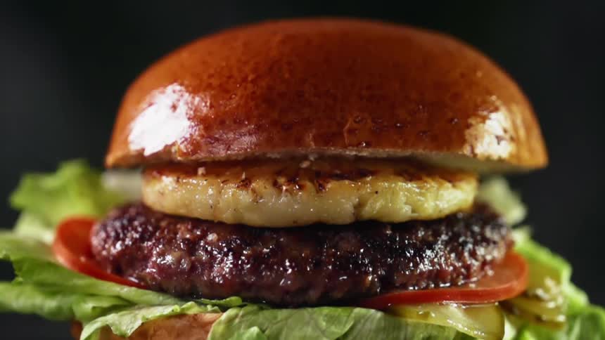 A gourmet burger with a slice of grilled pineapple, lettuce, tomato between a glistening brioche bun