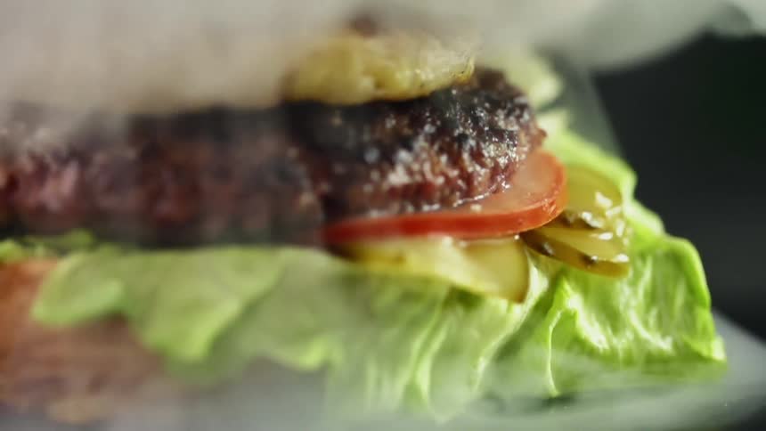 Transparent bowl lifts up releasing smoke and revealing a gourmet hamburger with a slice of grilled pineapple