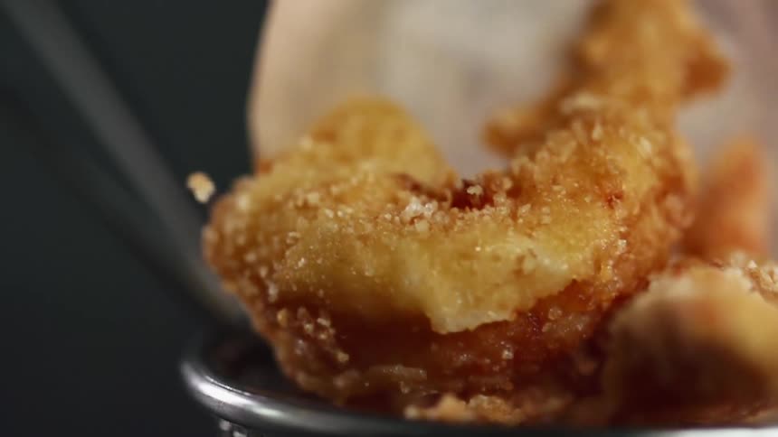 Fried shrimp covered in breadcrumbs falling into a basket