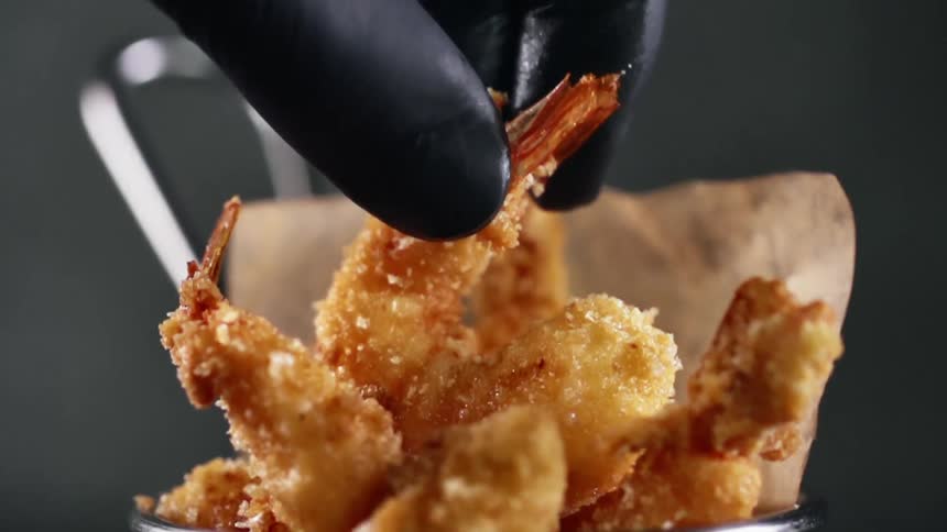A person with gloves picking up a fried shrimp from a basket