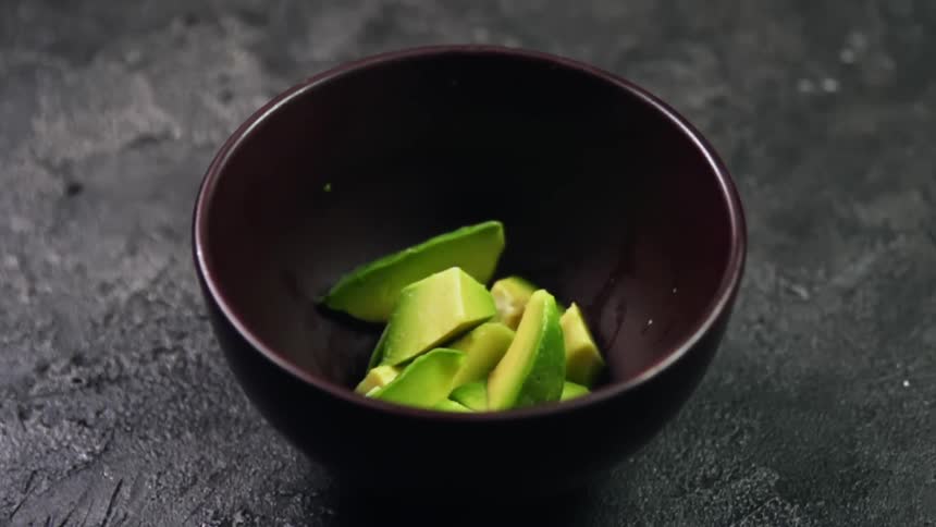 Chunks of ripe avocado being dropped in slow motion in a black bowl